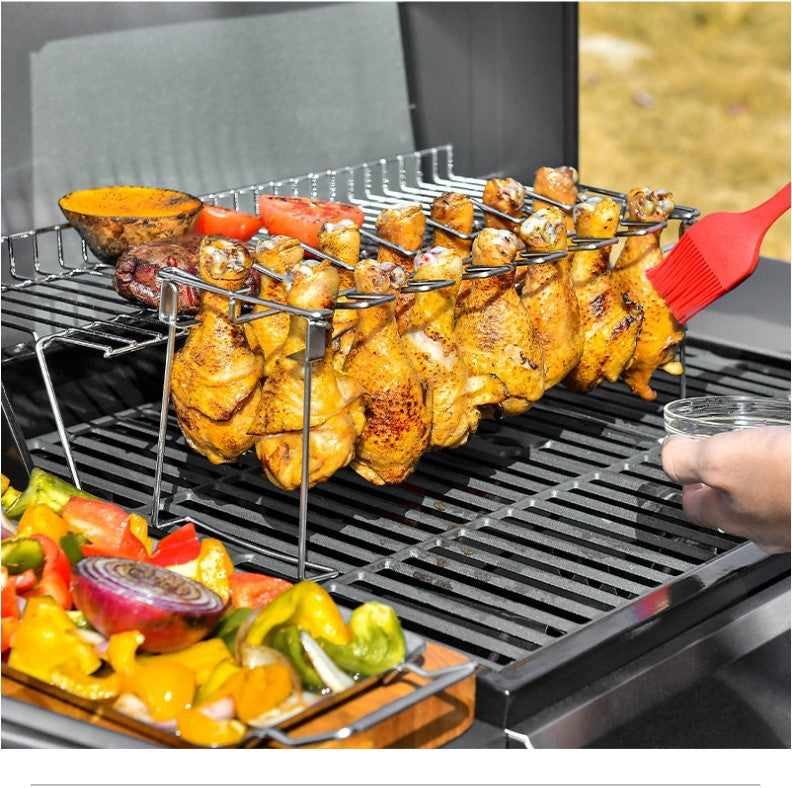 Trailblazer BBQ Rack 14-Slot Stainless Steel Masterpiece shown with drumsticks on the grill being basted with a red basting brush, grilled vegetables are to the left side