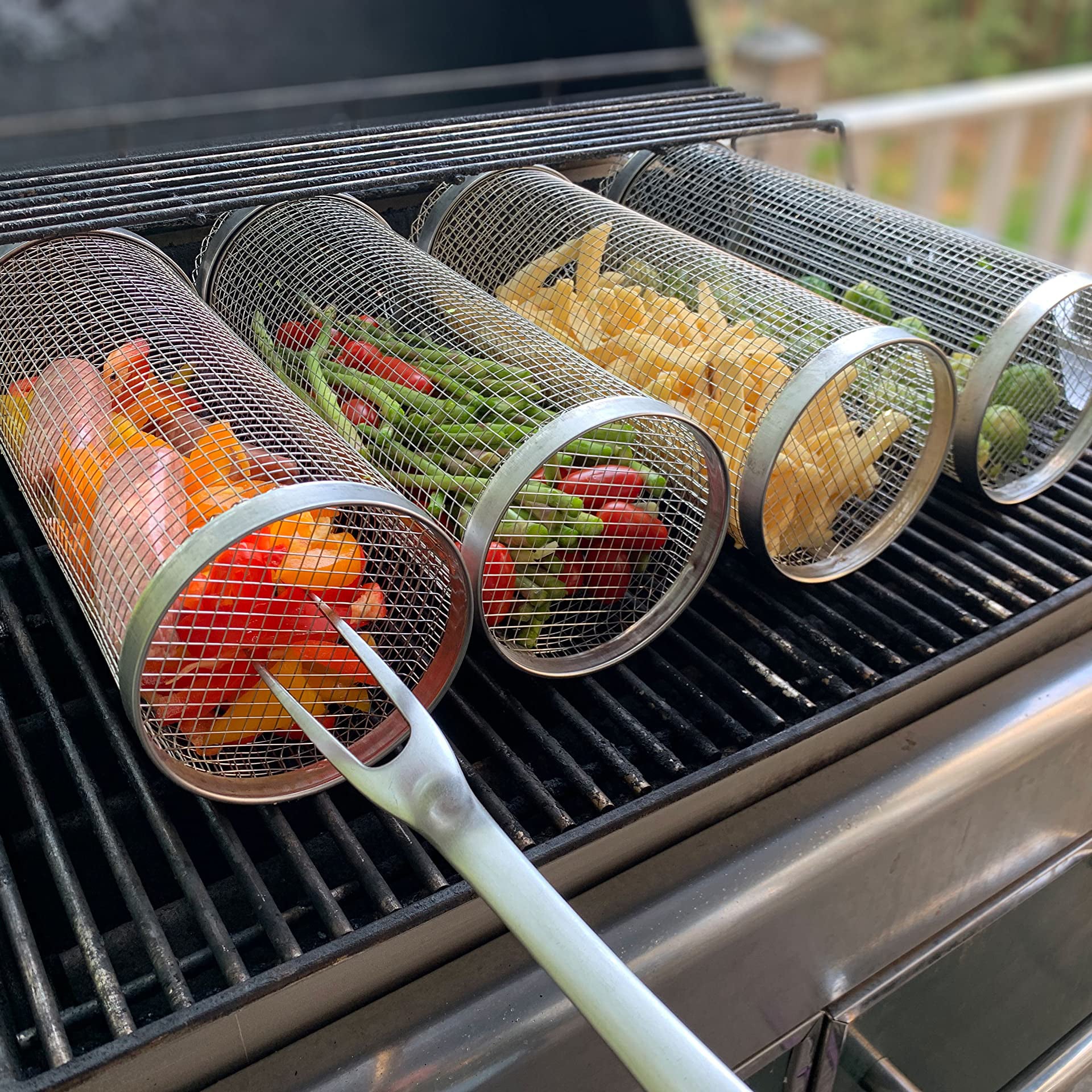 Campfire Companion Stainless Steel Grilling Basket on grill, with grill fork poking one.  Each has different food inside of them